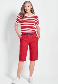 Haut en tricot rayé rouge, blanc et bleu ; associé à un short rouge arrivant aux genoux. Le mannequin porte des baskets blanches, avec les cheveux tombant sur les épaules.