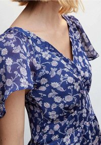 Robe bleue à fleurs avec des manches courtes évasées, présentant un décolleté en V et une texture à motifs de fleurs roses et de feuilles vertes.