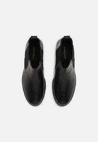 Pár černých kožených slip-on kotníkových bot s elastickými boky a poutky, zobrazených z výšky na bílém pozadí.