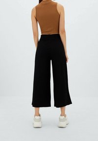 Bruine geribbelde mouwloze top gecombineerd met zwarte wijde geribbelde broek met hoge taille en zachte textuur, gedragen met witte sneakers.