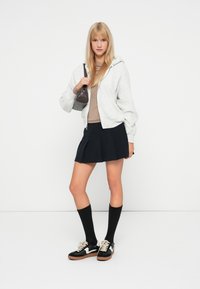Felpa grigia, top beige, gonna plissettata nera, calze nere fino al ginocchio e sneakers nere con dettagli bianchi. Piccola borsa grigia.