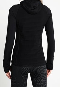 Black fitted hoodie with a textured, quilted back panel and long sleeves. Smooth hood and durable fabric with a sleek design.