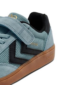Niebieski zamszowy i siateczkowy but sportowy z czarnymi akcentami, paskiem na rzep oraz gumową podeszwą z teksturowanym wzorem. Logo marki po boku.