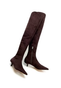 Brązowe zamszowe kozaki za kolano z noskami w szpic, niskim obcasem typu koci pazur, zamkiem błyskawicznym po boku i gładką fakturą. Wyróżniają się widocznymi przeszyciami.