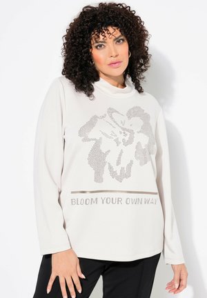 Helle beige Langarmshirt aus weichem Stoff, mit einem grafischen Blumenmotiv und dem Text "BLOOM YOUR OWN WAY" in metallischen Akzenten.