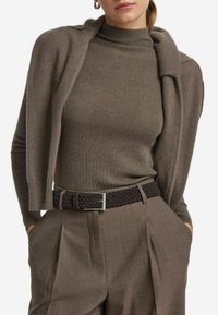 Bruine geribde coltrui gecombineerd met een bijpassende bruine cardigan, voorzien van een geweven zwart riem met een zilveren gesp. Tailored broek maakt de look compleet.