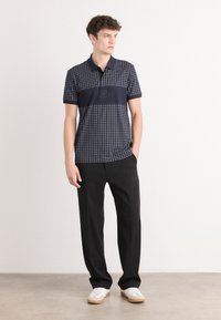 Námornícky polo s mriežkovým vzorom, krátke rukávy a čierny horizontálny panel; v kombinácii s čiernymi nohavicami a bielymi teniskami. Minimalistický dizajn.