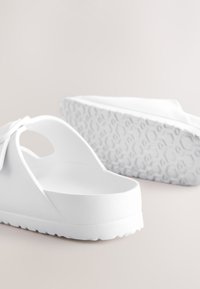 Sandales à enfiler blanches en plastique texturé, dotées d'une large bride, d'un bout ouvert et d'une semelle à motif hexagonal pour une meilleure adhérence.