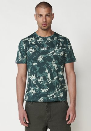 Tricou verde cu un model din bumbac; are un design abstract în nuanțe de verde deschis și închis; cu mâneci scurte și gât rotund.