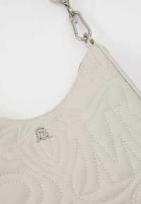Beige læder skuldertaske med præget svulmønster, der har sølvhardware og en aftagelig kædetræk, hvilket giver en struktureret finish.