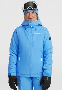 Lichtblauwe skijas met capuchon, ritszakken en logo-details. Gepaard met zwarte handschoenen en een blauwe muts, ontworpen voor wintersport.