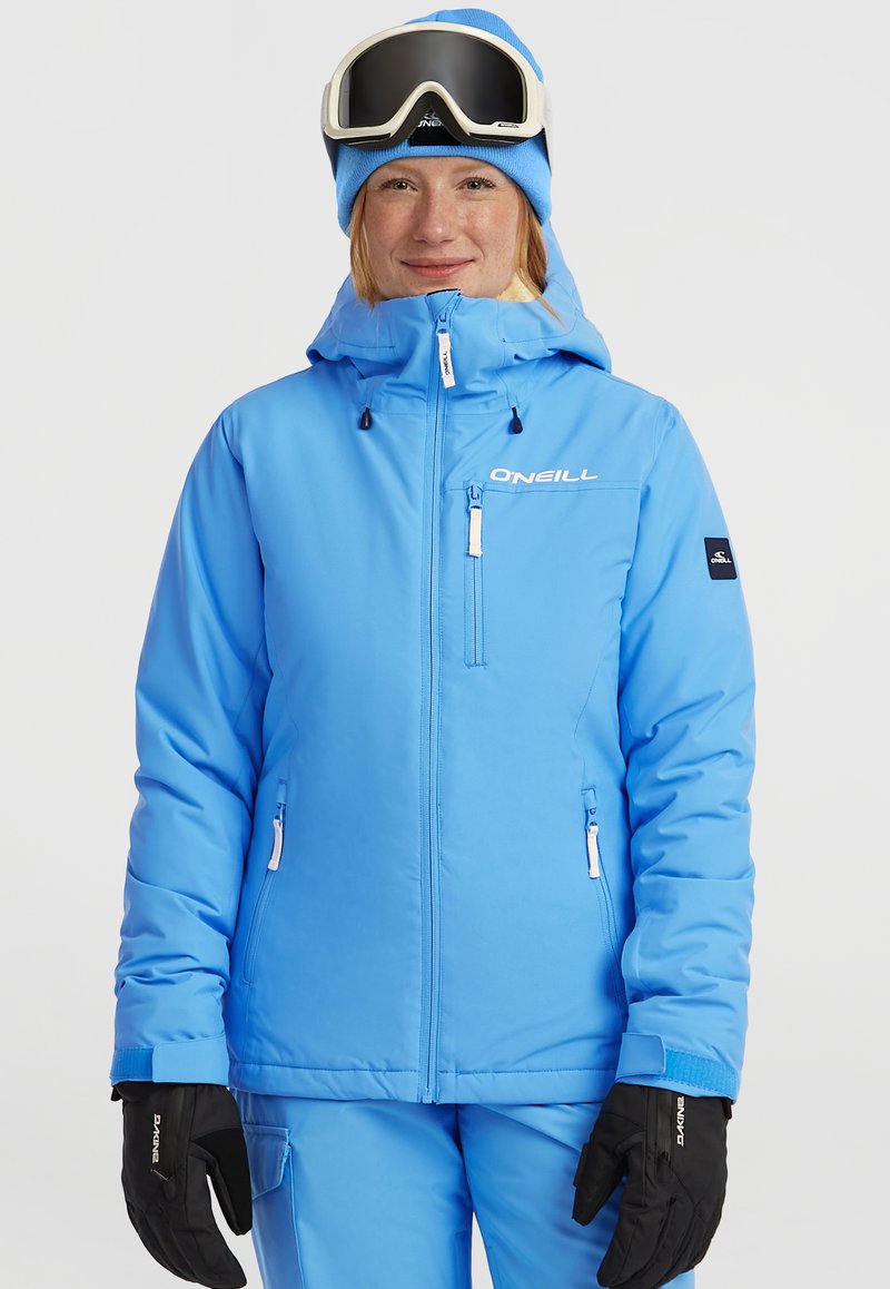 Lichtblauwe skijas met capuchon, ritszakken en logo-details. Gepaard met zwarte handschoenen en een blauwe muts, ontworpen voor wintersport.