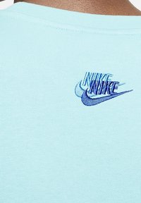 T-shirt di cotone blu chiaro con logo Nike ricamato in blu e tonalità di blu scuro sul retro vicino al colletto.