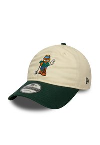 Gorra de béisbol beige con visera verde, que presenta un personaje de golfista bordado. Correa ajustable en la parte trasera, tejido texturizado en la visera.