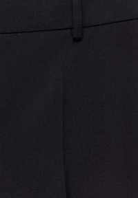 Čierne nohavice na mieru vyrobené z textúrovaného materiálu. Obsahujú plochý predný diel s úzkym pásom a minimálnymi švami.