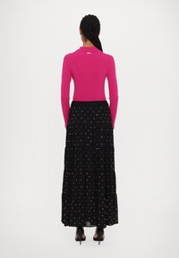 Fuchsia långärmad topp möter en svart plisserad kjol med vita prickar. Kjolen har ett elastiskt midjeband och en flödande silhuett.