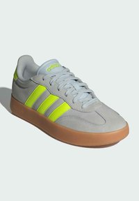 Grey suede athletic shoe with three bright yellow stripes, light blue laces, and a tan rubber sole. Rounded toe, minimalistic design.