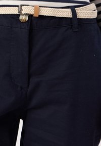 Námořnické modré kalhoty s tkaným béžovým páskem a hnědým akcentem. Obsahují zapínání na knoflík a jemnou texturu látky.