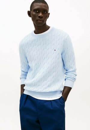 Maglione azzurro chiaro a trecce con polsini e orlo a coste, con un piccolo logo sul petto sinistro, abbinato a pantaloni blu navy.