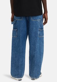 Pantalones cargo de denim azul de corte wide fit con dos grandes bolsillos laterales, un tejido texturizado y detalles de costura visibles.