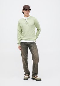 Light green long-sleeve shirt with three buttons, layered over a white T-shirt. Brown cap, faded gray jeans, and multi-colored shoes.