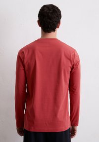 Langsleeve shirt in roestbruin katoen met een ronde hals, gladde textuur en een losse pasvorm. Bevat eenvoudige stiksels op de zoom.