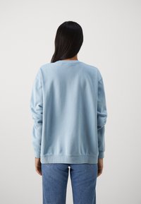 Sudadera de algodón de cuello redondo en azul claro, con puños y dobladillo de canalé, combinada con jeans de denim azul, vista desde la parte de atrás.