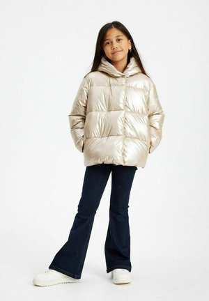 Giacca a vento metallizzata beige, con cappuccio, design trapuntato e vestibilità rilassata. Abbinata a jeans scuri a zampa d'elefante e sneakers bianche.