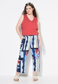 Top rosso senza maniche abbinato a pantaloni cropped a fantasia blu, rossi e crema, caratterizzati da un mix di righe e designs astratti. Tessuto morbido.