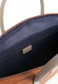 Bruine en beige handtas met een marineblauwe binnenkant, voorzien van een ritsafsluiting, een gladde textuur en een metalen logo-tag.