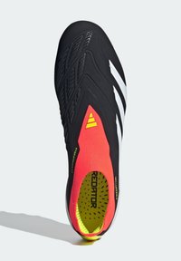 Svart fotbollssko med en snug röd stickad krage. Har vita ränder, texturerad svart ovandel och en ljusgul innersula med svarta prickar.