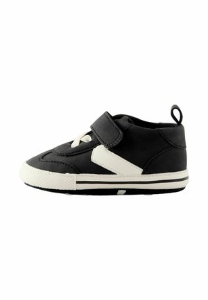 Basket bébé noire avec semelle blanche, lacets blancs et une bride noire en Velcro, vue de côté sur fond blanc.
