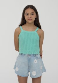Un top lavorato a maglia verde menta con bordi ondulati e spalline sottili, abbinato a dei pantaloni shorts in denim azzurro chiaro decorati con applicazioni di fiori bianchi.