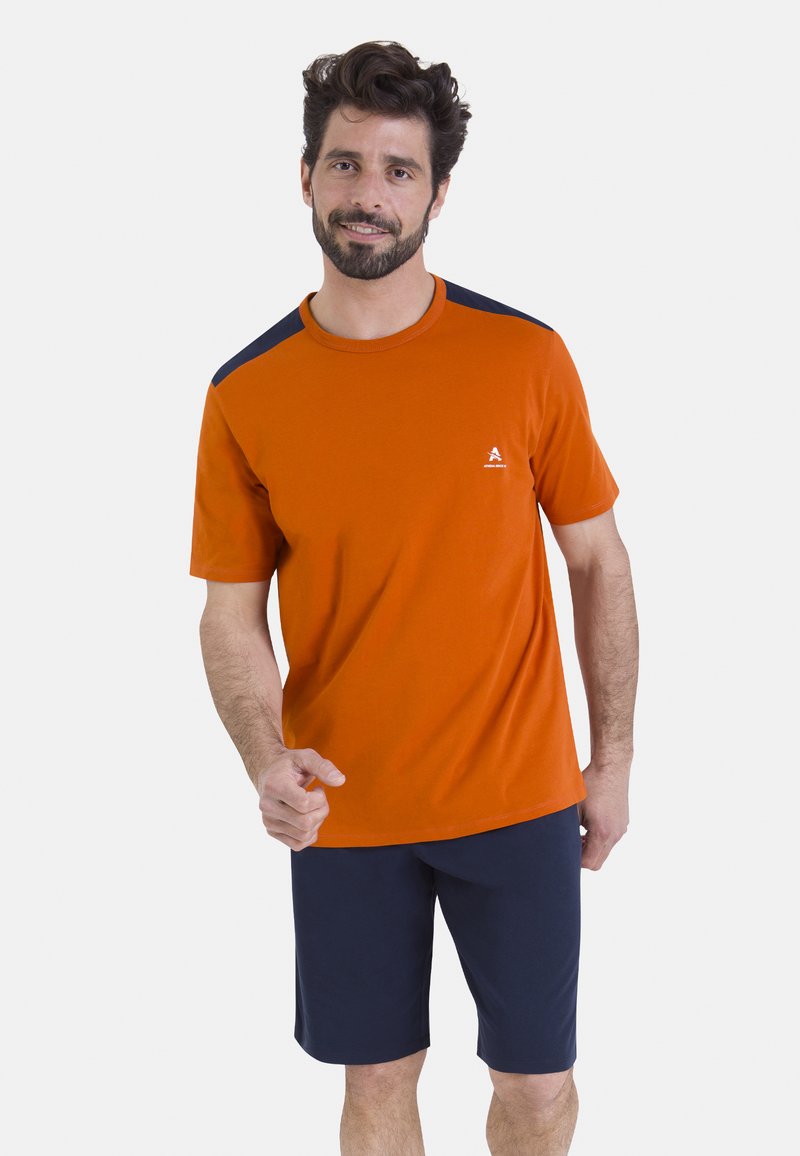 T-shirt orange à manches courtes avec des accents bleu marine sur les épaules, associé à un short bleu marine. Confectionné en tissu doux, avec un logo sur la poitrine.