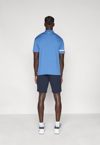 Μπλε πόλο πουκάμισο με κοντά μανίκια, με λεπτομέρεια λευκής ρίγας. Συνδυάζεται με ναυτικό σορτς και λευκά αθλητικά παπούτσια. Λείο ύφασμα και casual εφαρμογή.