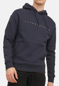 Dunkelblaues Hoodie aus Baumwollmischung, ausgestattet mit einer Kängurutasche und goldfarbenem "JACK & JONES"-Schriftzug auf der Brust, mit verstellbaren Kordeln.