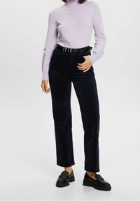 Marineblauwe corduroy broek met rechte pijpen en voorzakken, gecombineerd met een lichtpaarse coltrui en zwarte platform loafers, afgewerkt met een zwarte riem.