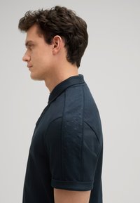 Navyblaues Poloshirt mit strukturiertem Design auf den Schultern, ausgestattet mit einem klassischen Kragen und kurzen Ärmeln, gefertigt aus weichem Baumwollmaterial.