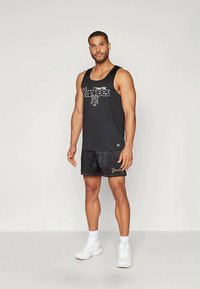 Camiseta sin mangas negra con gráfico de "New York Yankees", combinada con shorts negros con acentos dorados. Modelo lleva zapatillas blancas.