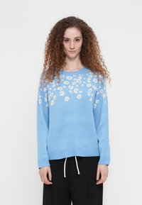 Φωτεινό γαλάζιο πλεκτό πουλόβερ με σχέδιο λεοπάρδαλης σε λευκό. Χαλαρή εφαρμογή, στρογγυλή λαιμόκοψη και ριμπ μανσέτες. Συνδυασμένο με μαύρο παντελόνι.