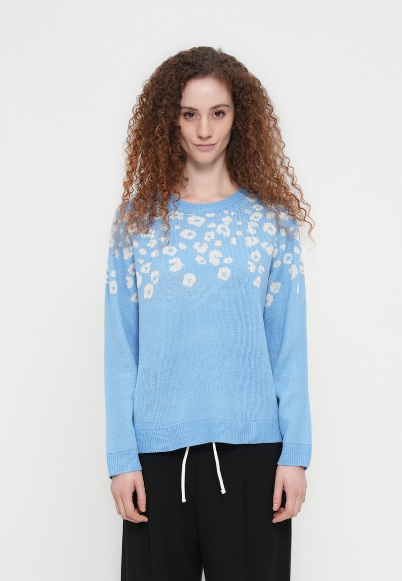 Φωτεινό γαλάζιο πλεκτό πουλόβερ με σχέδιο λεοπάρδαλης σε λευκό. Χαλαρή εφαρμογή, στρογγυλή λαιμόκοψη και ριμπ μανσέτες. Συνδυασμένο με μαύρο παντελόνι.