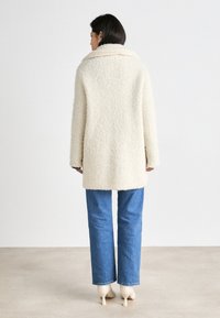 Cream-colored, fluffy coat with a wide collar and long sleeves, paired with light blue denim jeans and beige pointed heels.
