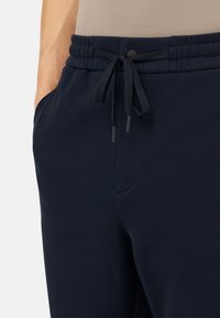 Jūras spēku jogger bikses ar teksturētu apdari, elastīgu jostu un auklu. Iespējami sānu kabatas un plūstoša piegriezuma.