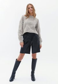 Maglione lavorato a maglia grigio chiaro con motivo a foglia, pantaloni shorts neri in pelle e stivali neri alti. Tessuto liscia e vestibilità rilassata.