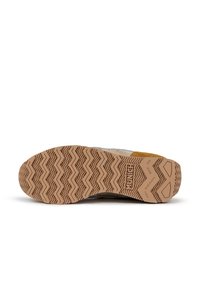 Sneaker sole features a zigzag tread pattern in beige rubber, with a brown accent near the heel and branding on the side.
