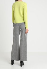 Ljusgul tröja med rund halsringning, i kombination med grå houndstooth-mönstrade vida byxor och svarta blockklackade stövlar.