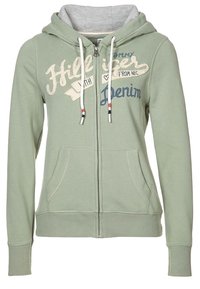 Zelená mikina s kapucí na zip z měkké tkaniny, s šedým vnitřkem, předními kapsami a vytištěným textem v krémové a námořnické modři. Ozdobená stahovacími šňůrkami.