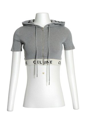 Sweat à capuche court gris manches courtes avec fermeture éclair devant, cordons et bande élastique blanche à l'ourlet avec texte noir "CELINE" sur un mannequin blanc.