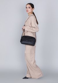 Borsa a tracolla in pelle nera con una texture liscia, design trapuntato e dettagli borchiati, indossata crossbody con una lunga tracolla.