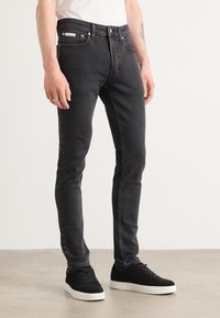 Pantalones vaqueros negros ajustados de denim, con un diseño clásico de cinco bolsillos, remaches de metal y una sutil etiqueta de la marca en la cinturilla.